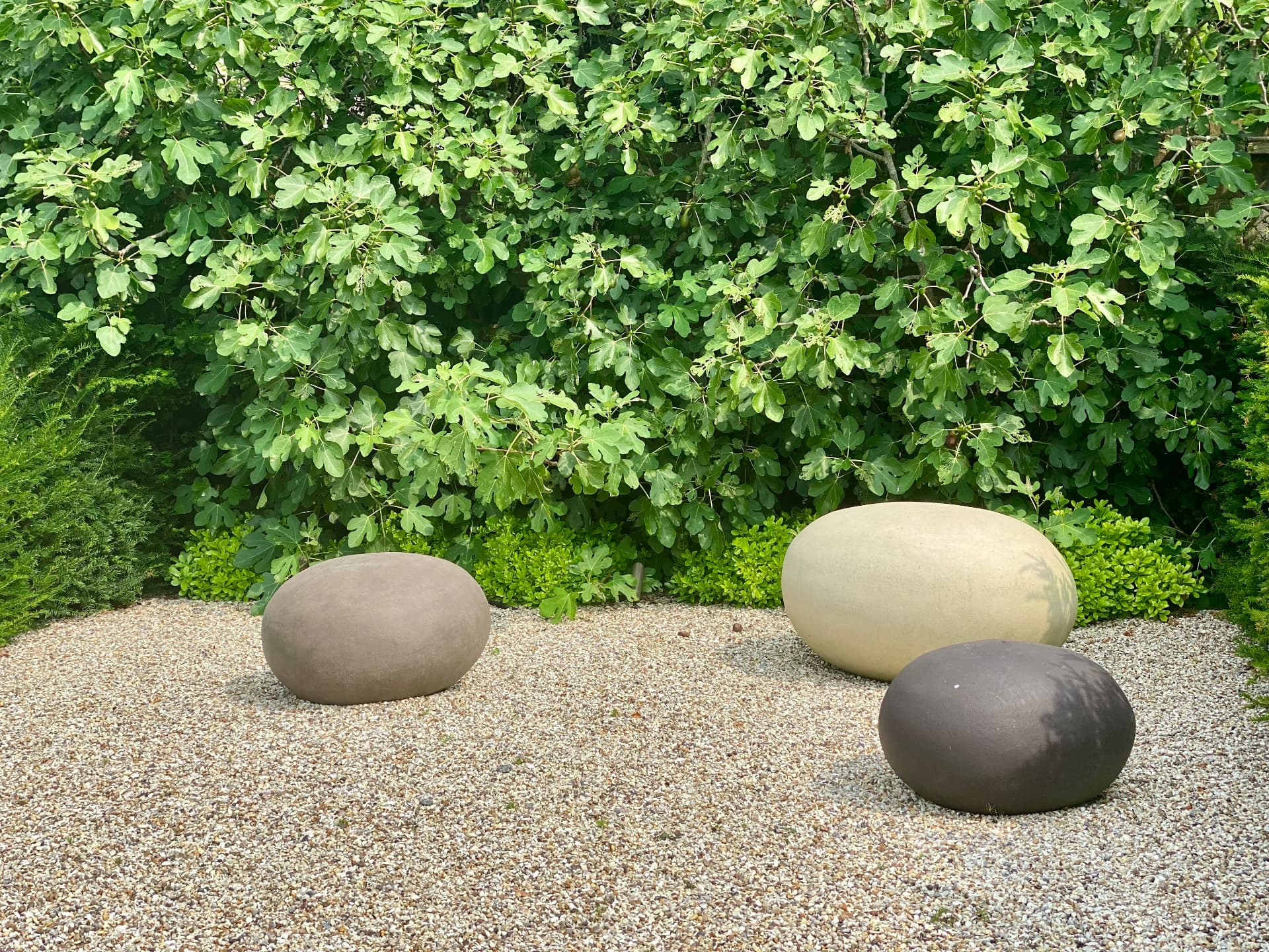 Three sculptural rounded stone forms set in gravel against a green hedge