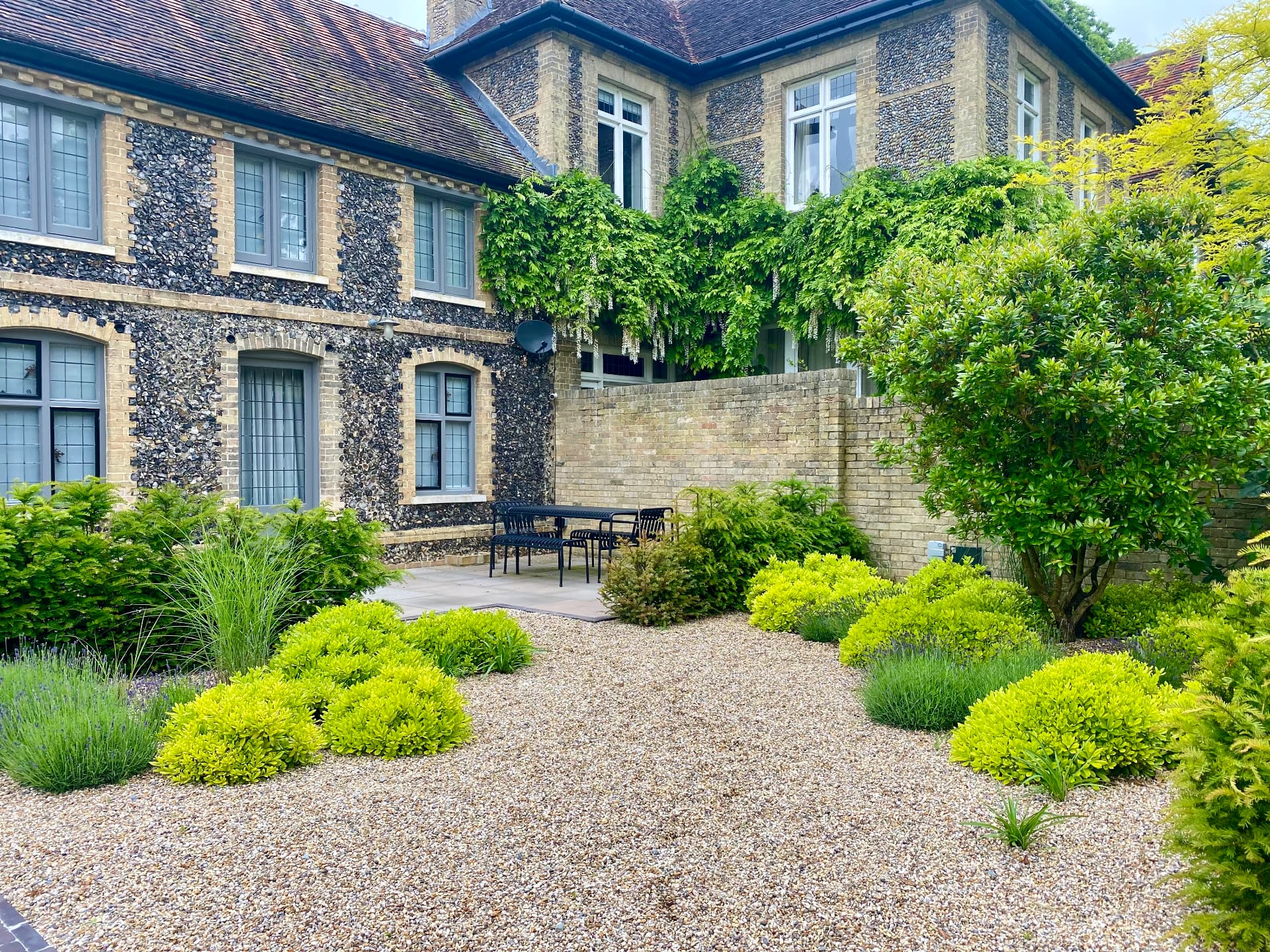 Flint cottage with gravel courtyard, clipped planting and sheltered dining area