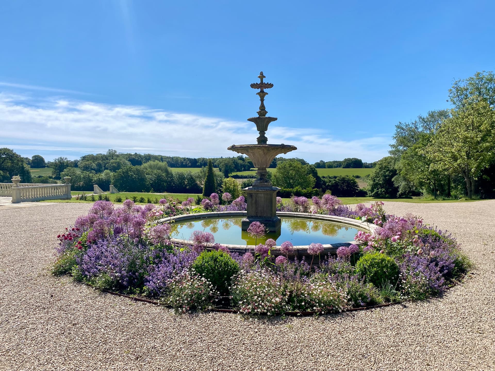 Circular fountain with richly layered planting, gravel terraces and open Suffolk countryside beyond