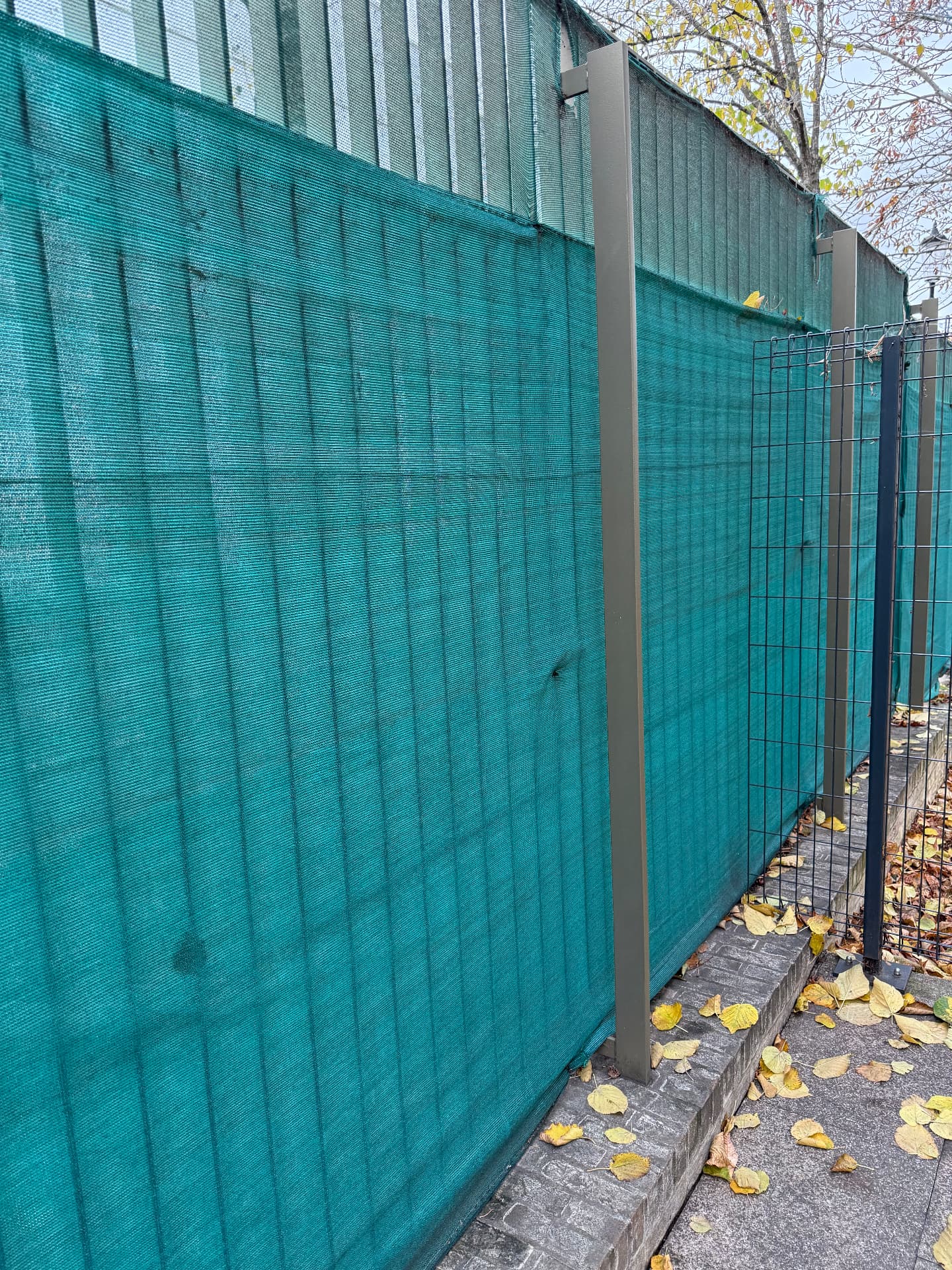 Green screening mesh fixed to the perimeter fencing, sagging between the posts