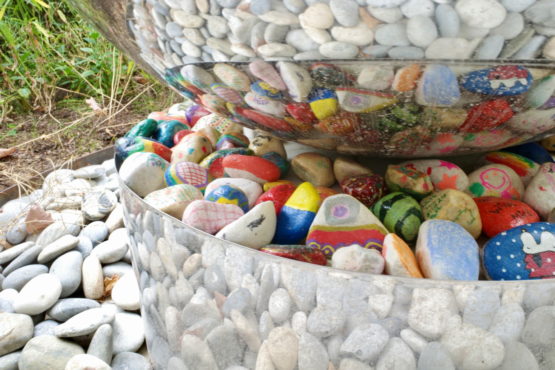 Painted pebbles collected in a stone-clad water bowl within the pebble river