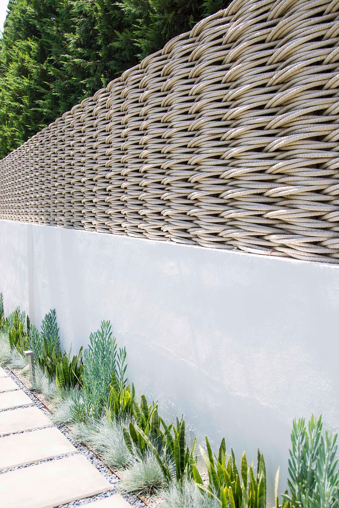 Bespoke woven screening above a white rendered wall with narrow architectural planting at its base