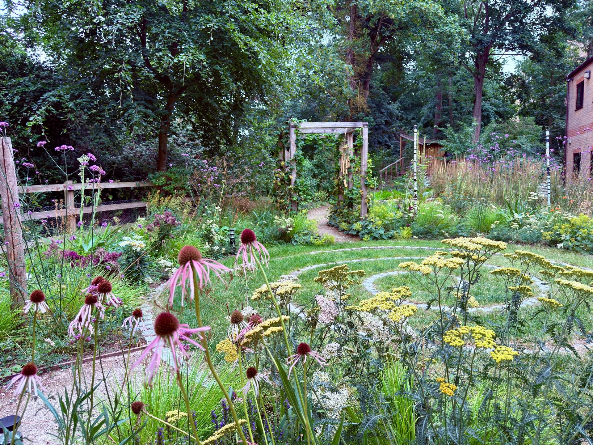 Layered flowering planting around the circular meditative lawn beneath mature trees
