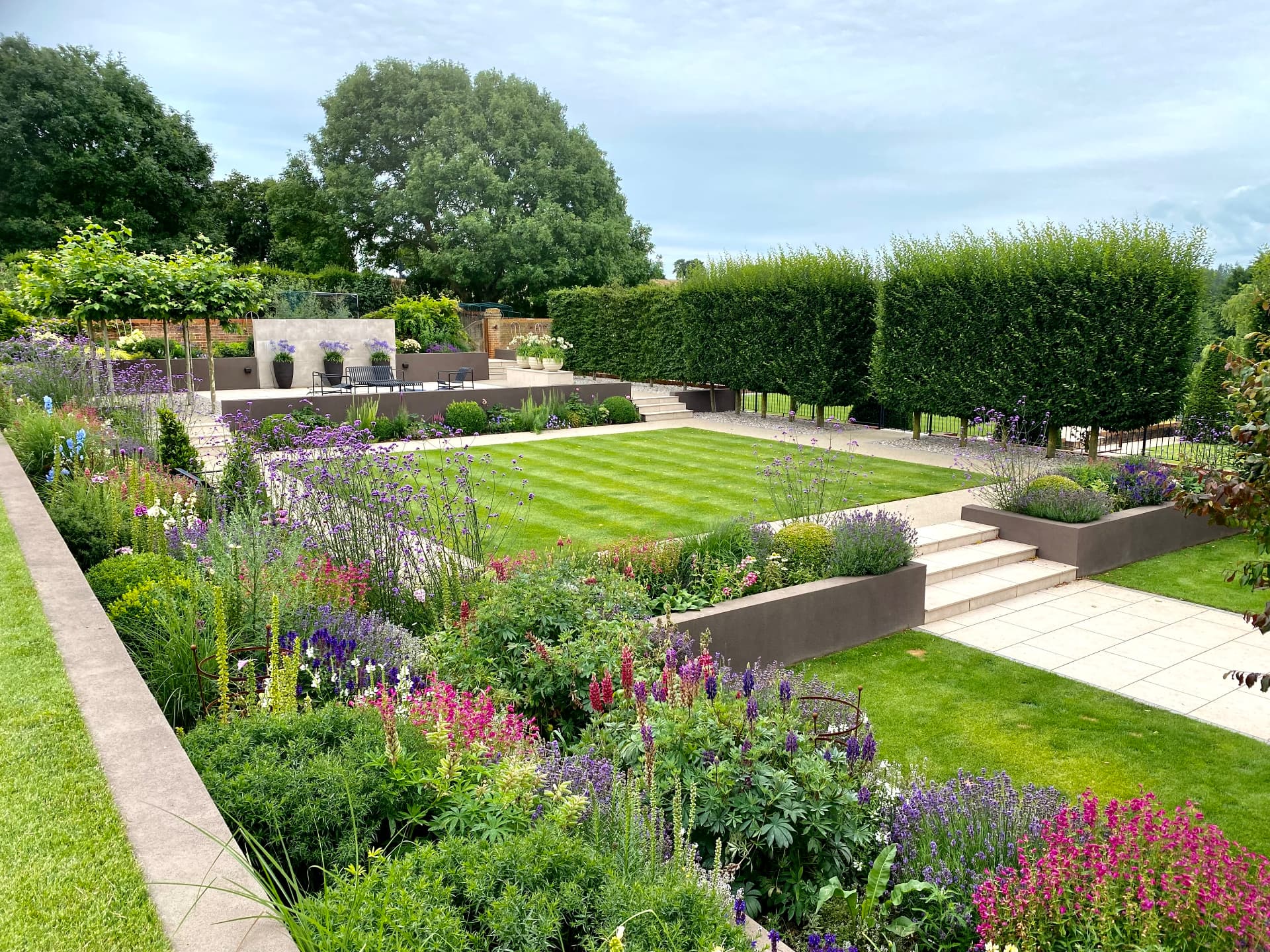 Terraced country garden with central rectangular lawn, layered planting, clipped hedging and upper terrace beyond