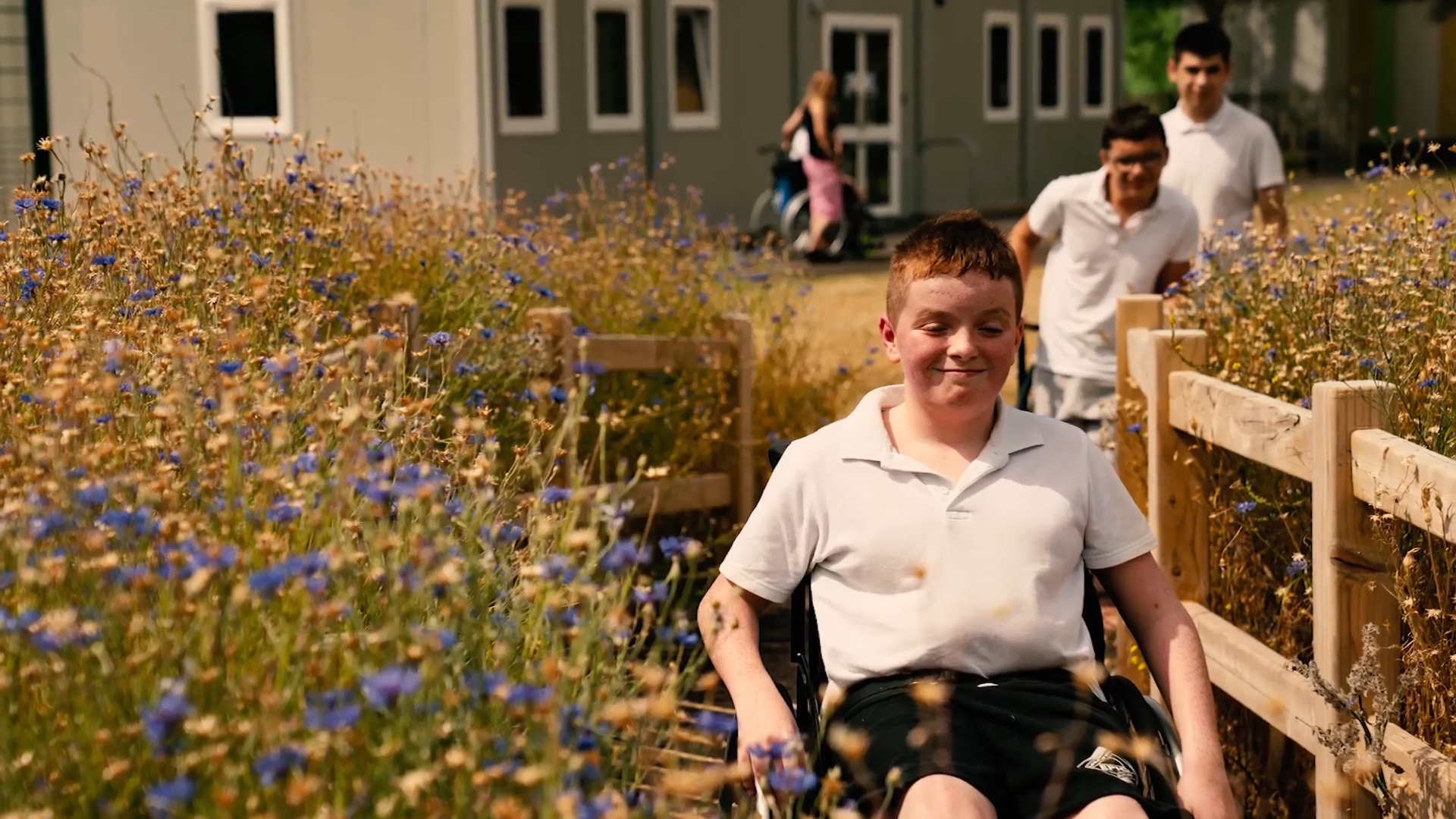 Young wheelchair user travelling along a timber bridge through flowering meadow planting