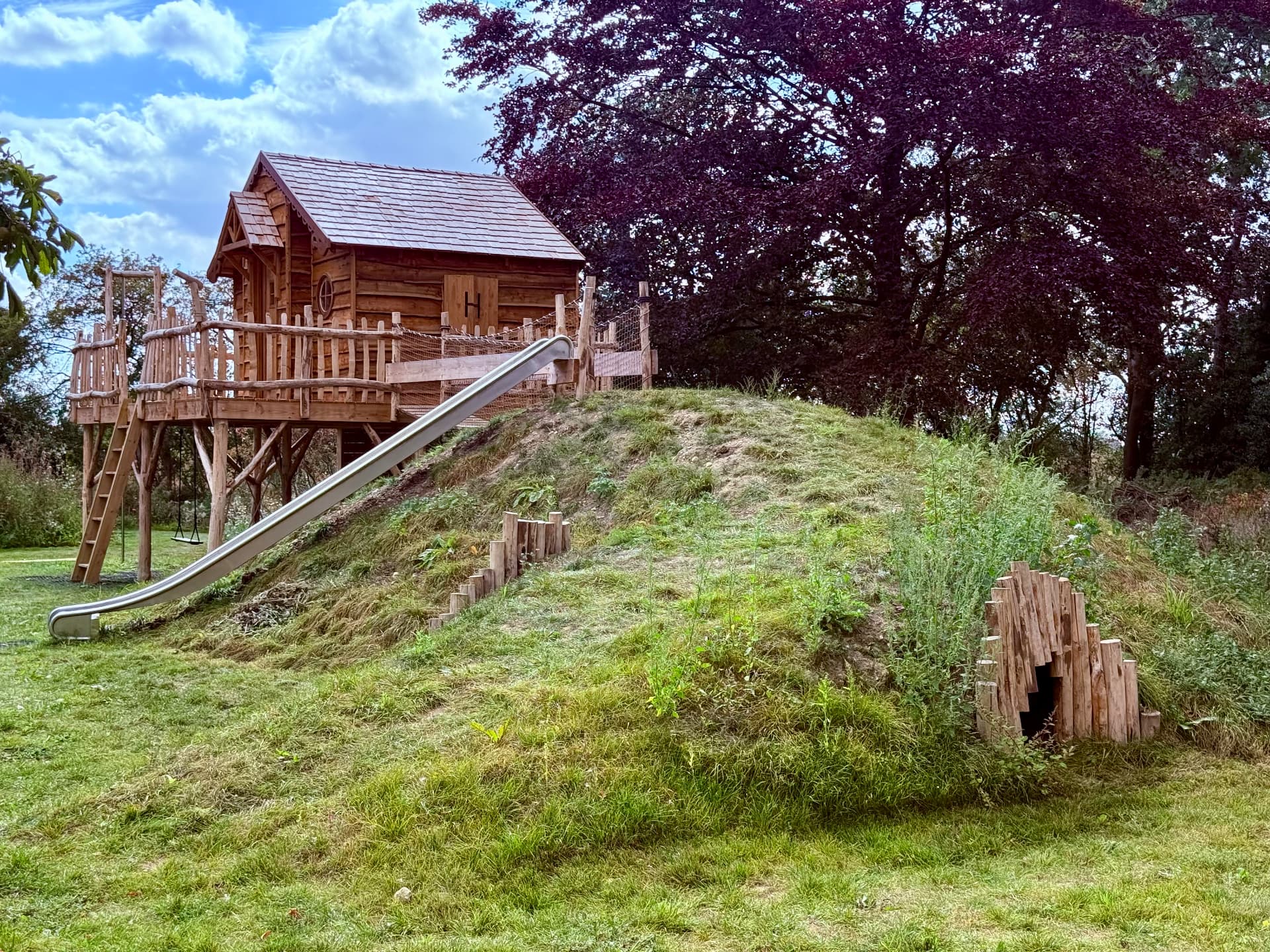 Bespoke timber playhouse integrated into a planted landform with slide and tunnel