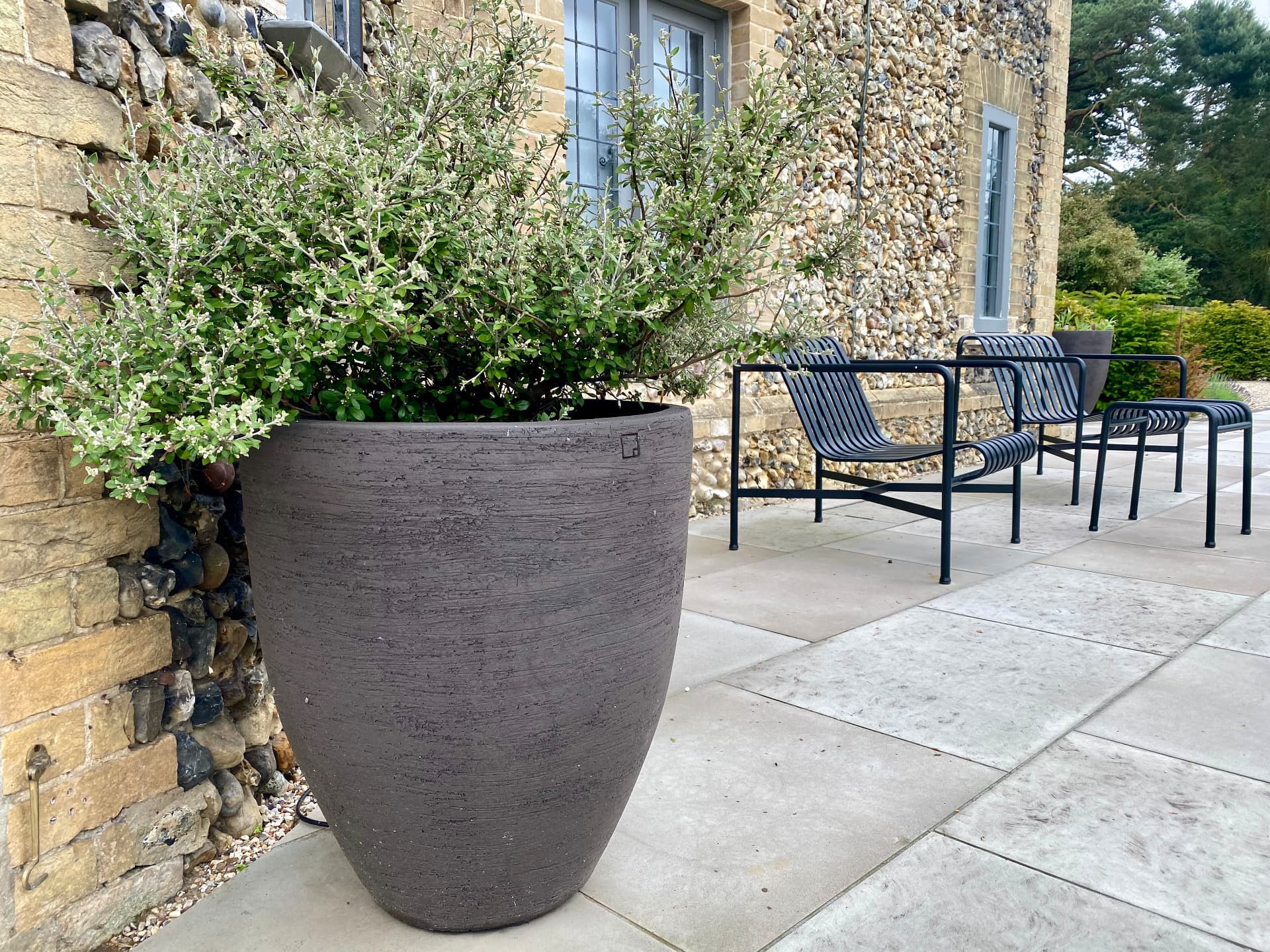Large dark planter beside the flint wall with outdoor dining furniture on the terrace
