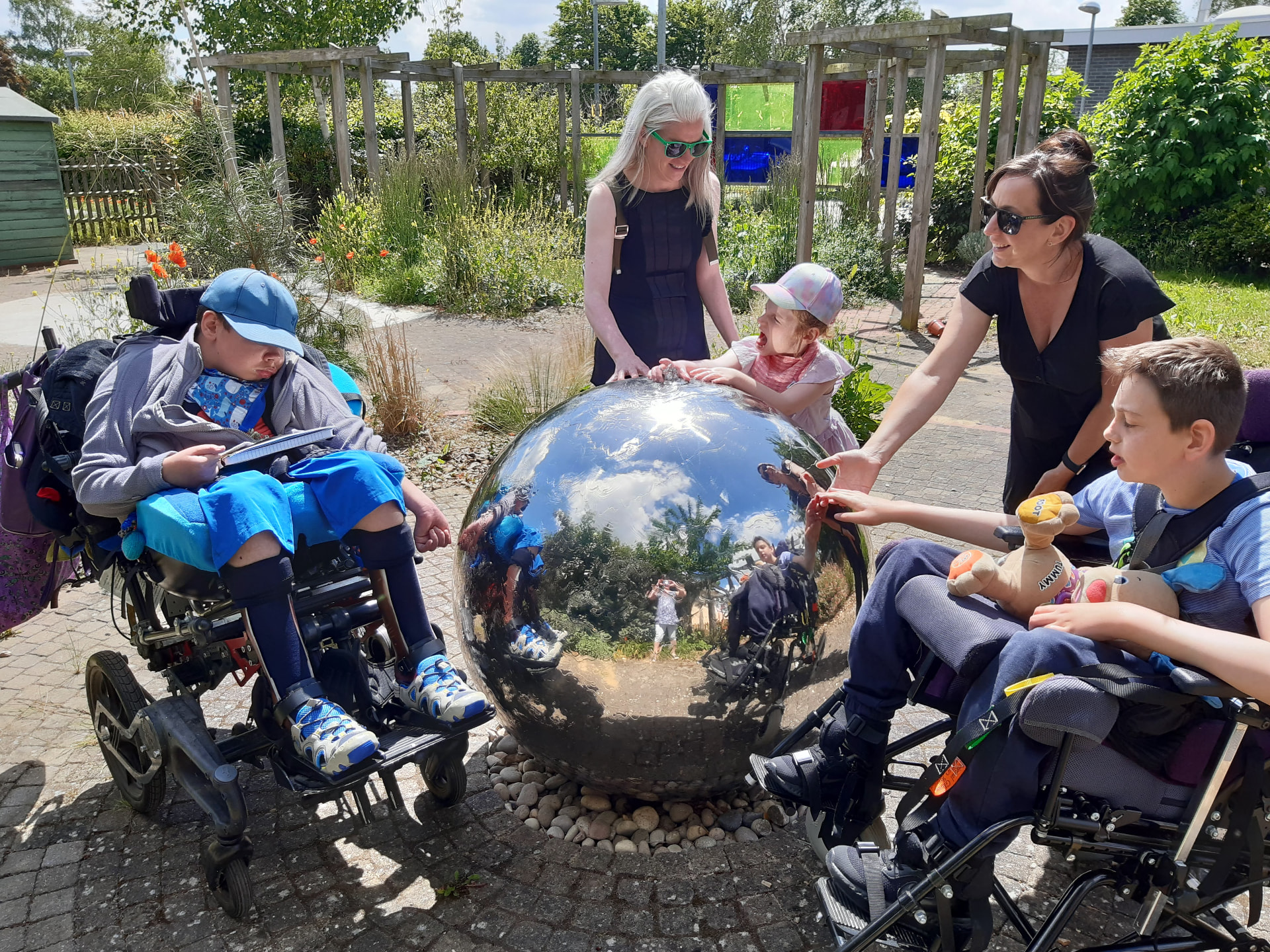 Pupils, wheelchair users and staff interacting with a reflective stainless-steel sphere in the sensory garden