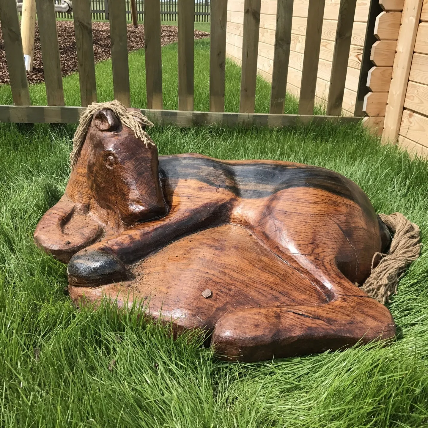 Carved wooden horse sculpture resting in long grass