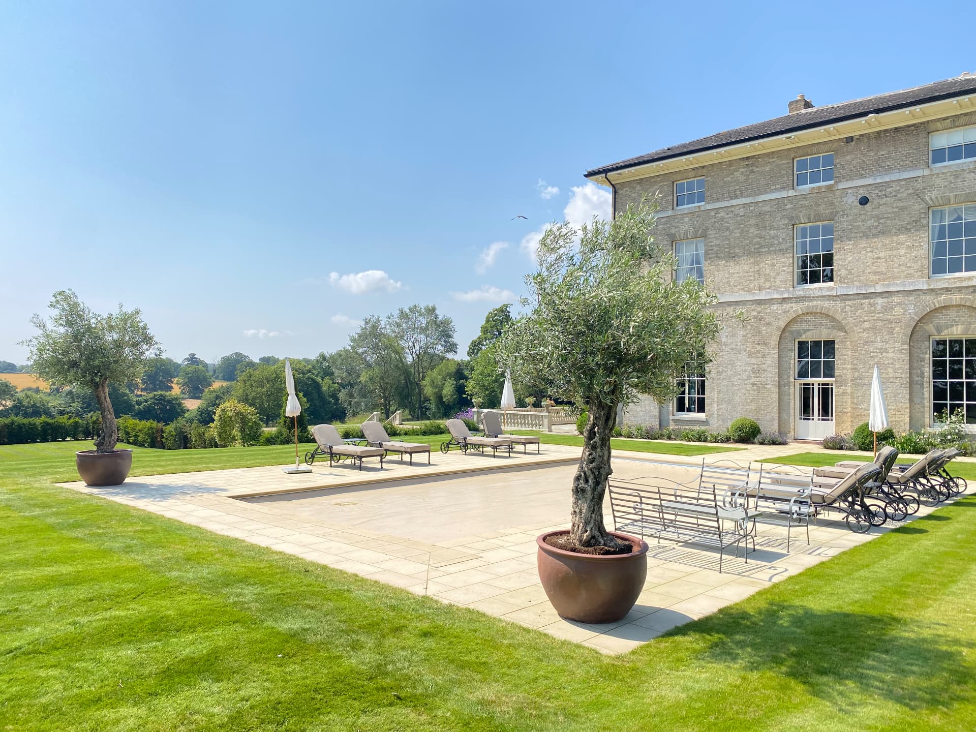 House terrace with outdoor furniture, planted pots, lawn and countryside beyond