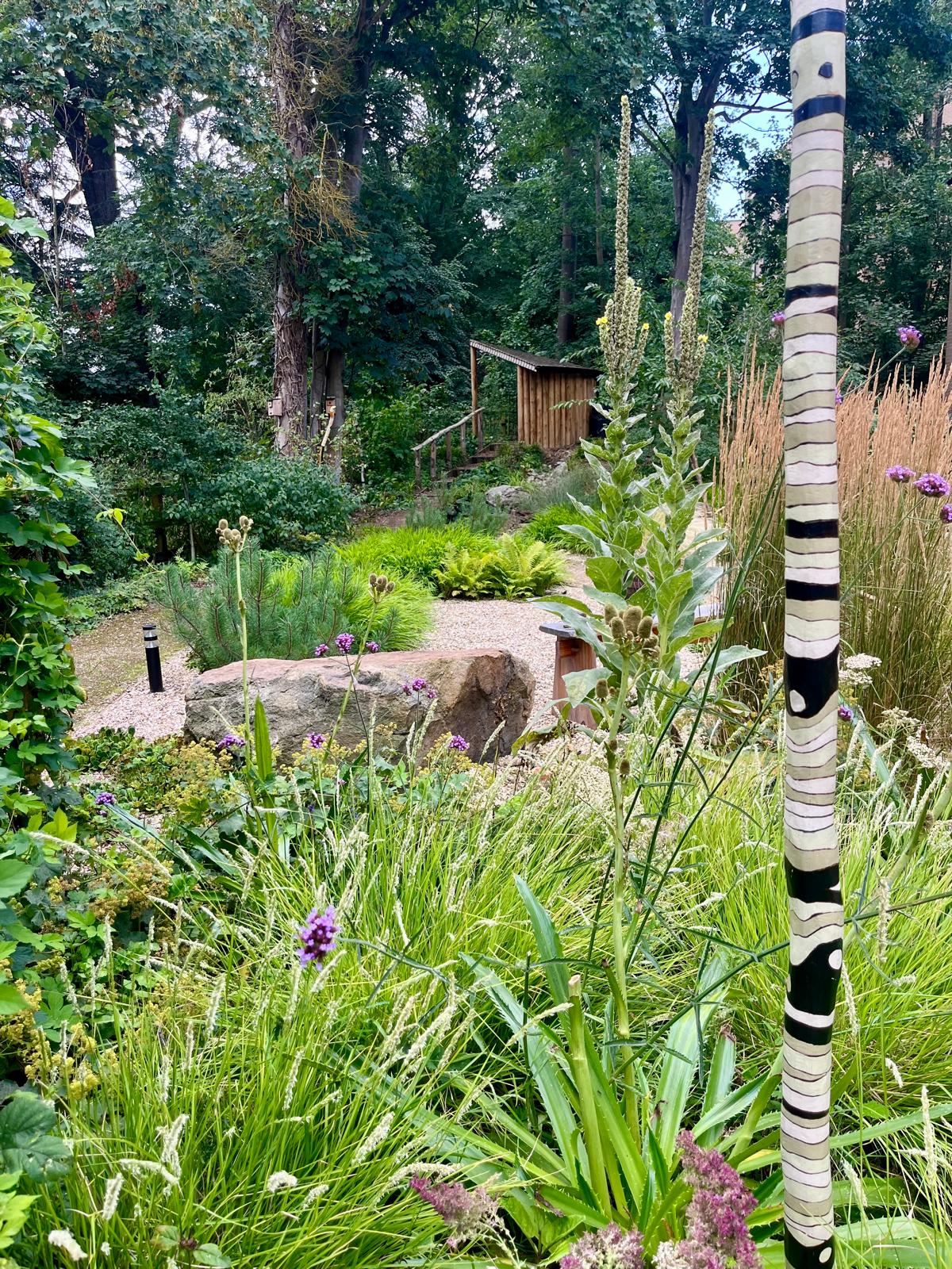 Immersive woodland planting with a striped vertical sculpture and sheltered garden path