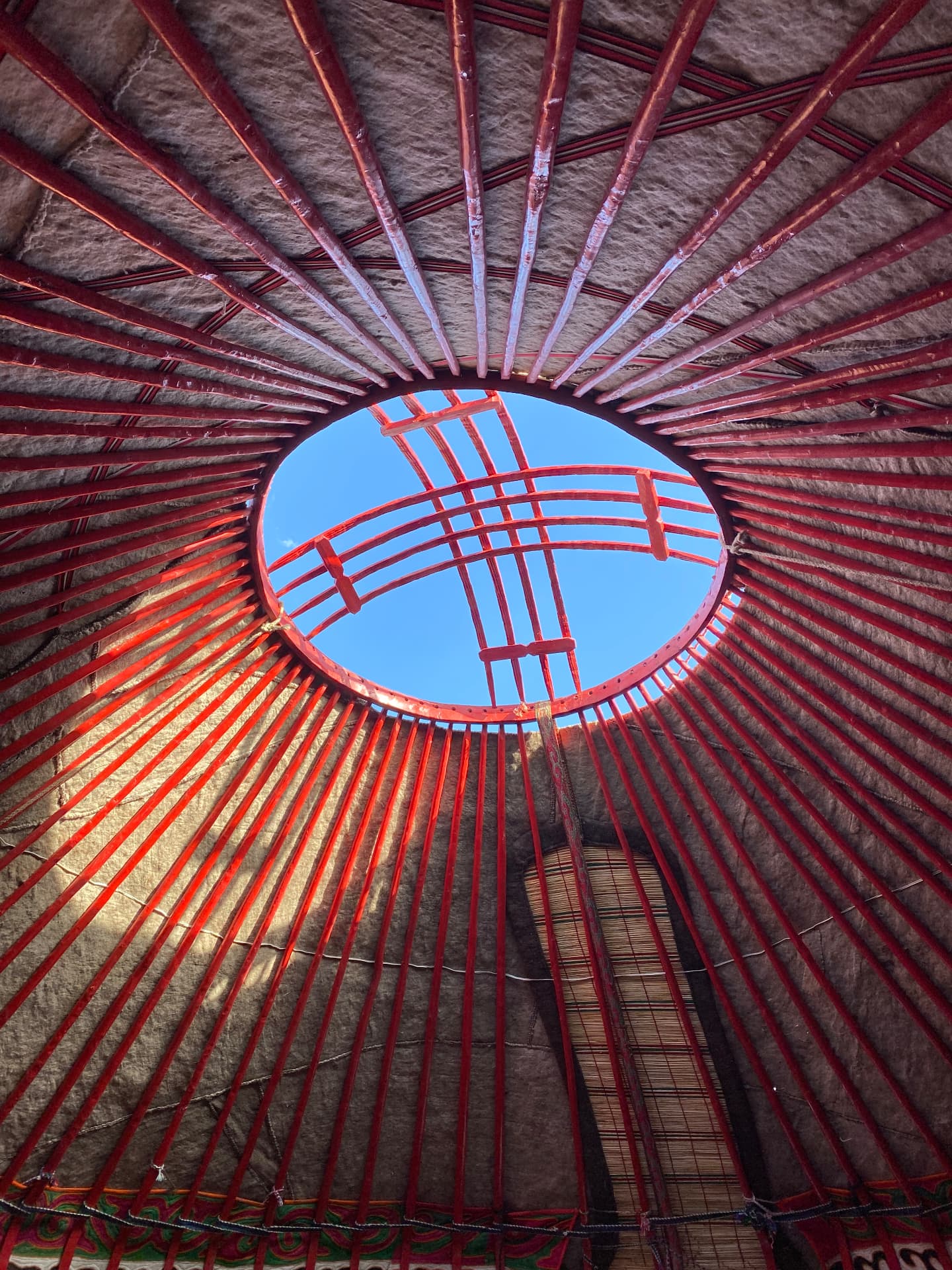 Interior of a yurt looking up through the red crown wheel to blue sky