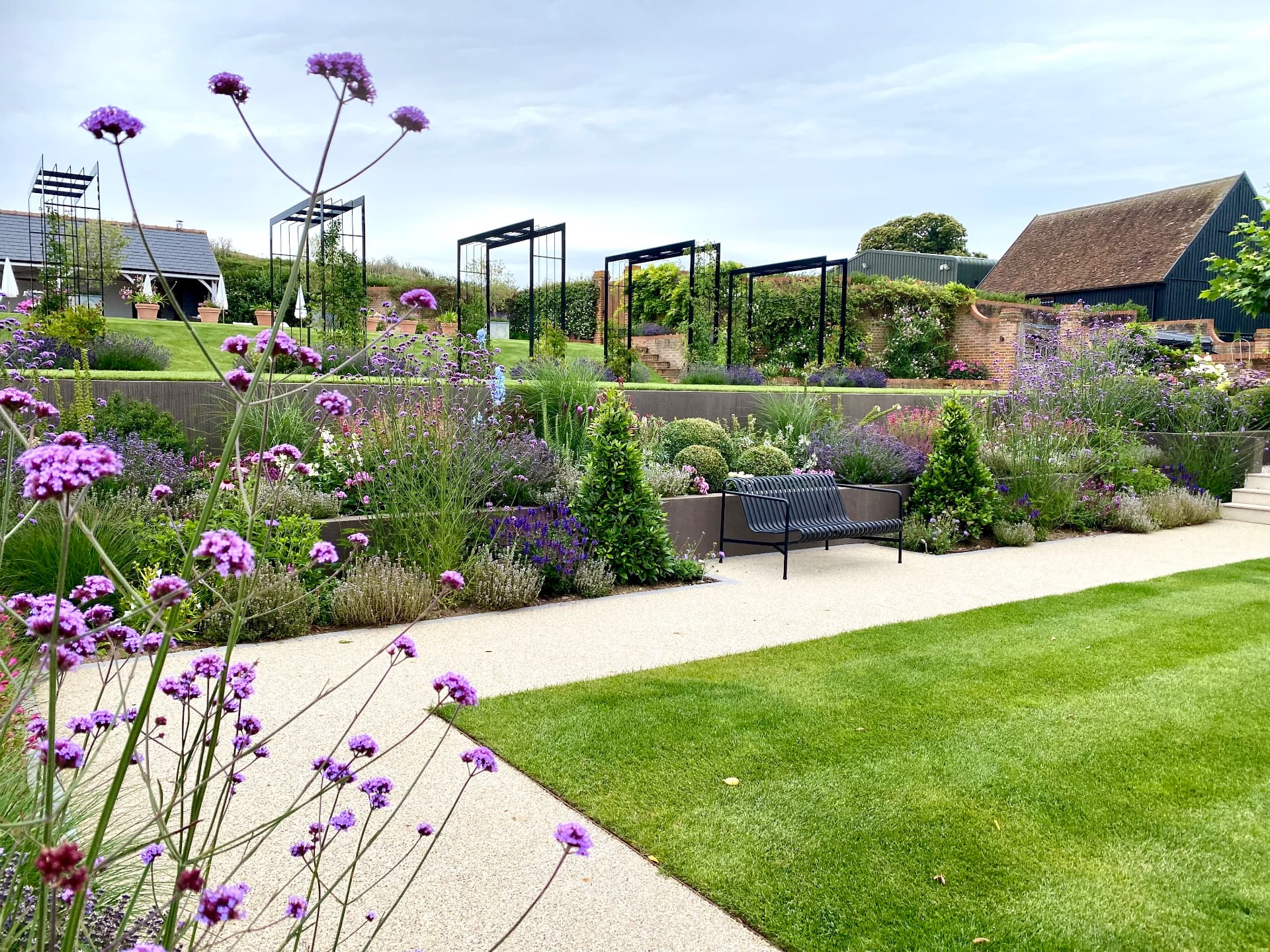 Verbena in the foreground with lawn, seating, terraces and garden structures beyond