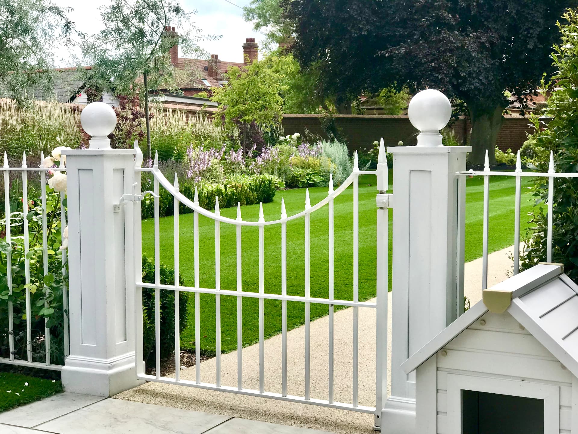 Bespoke white gate and balustrade opening onto lawn and layered planting