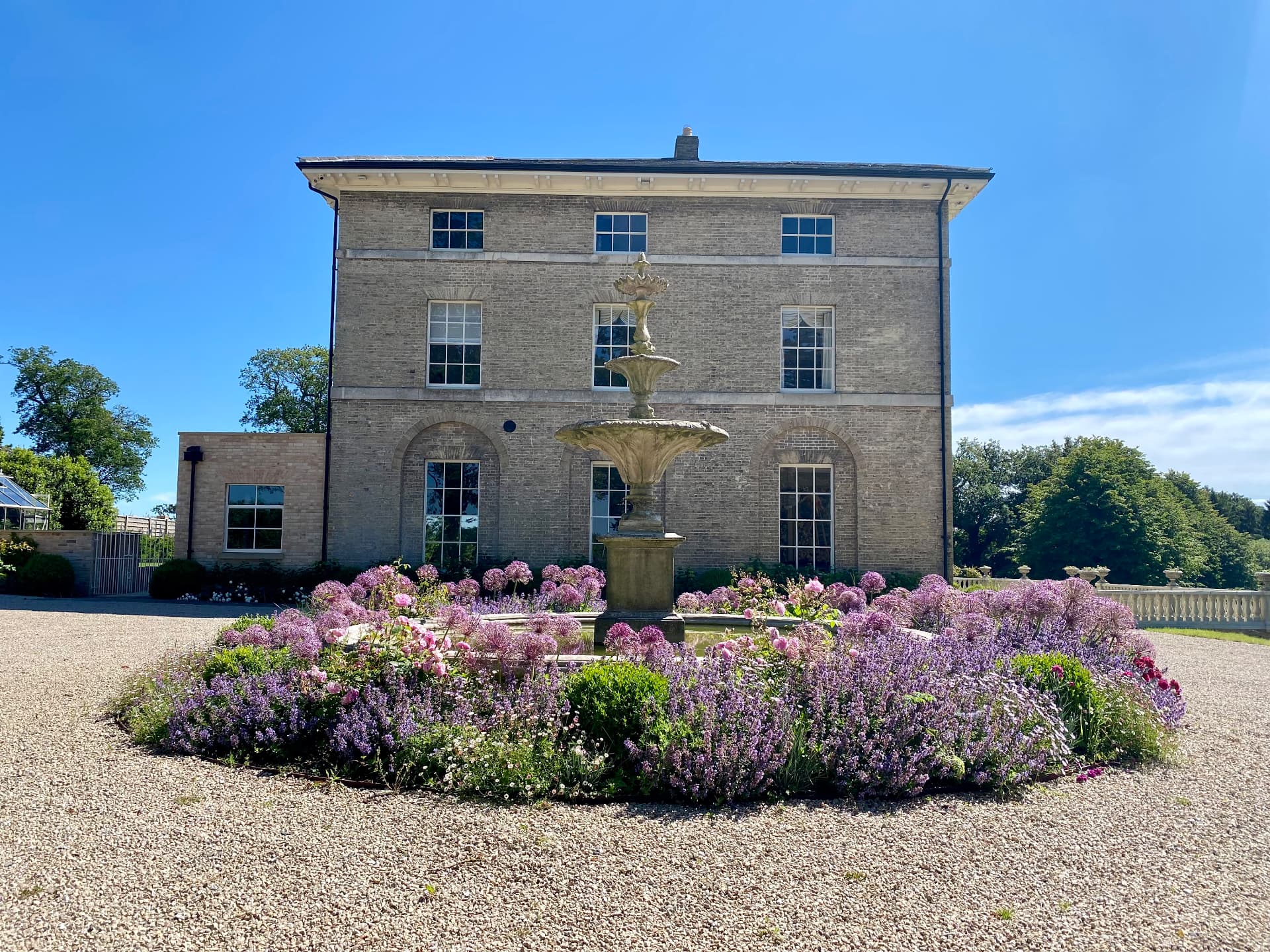 Principal house elevation beyond a circular fountain and flowering planting
